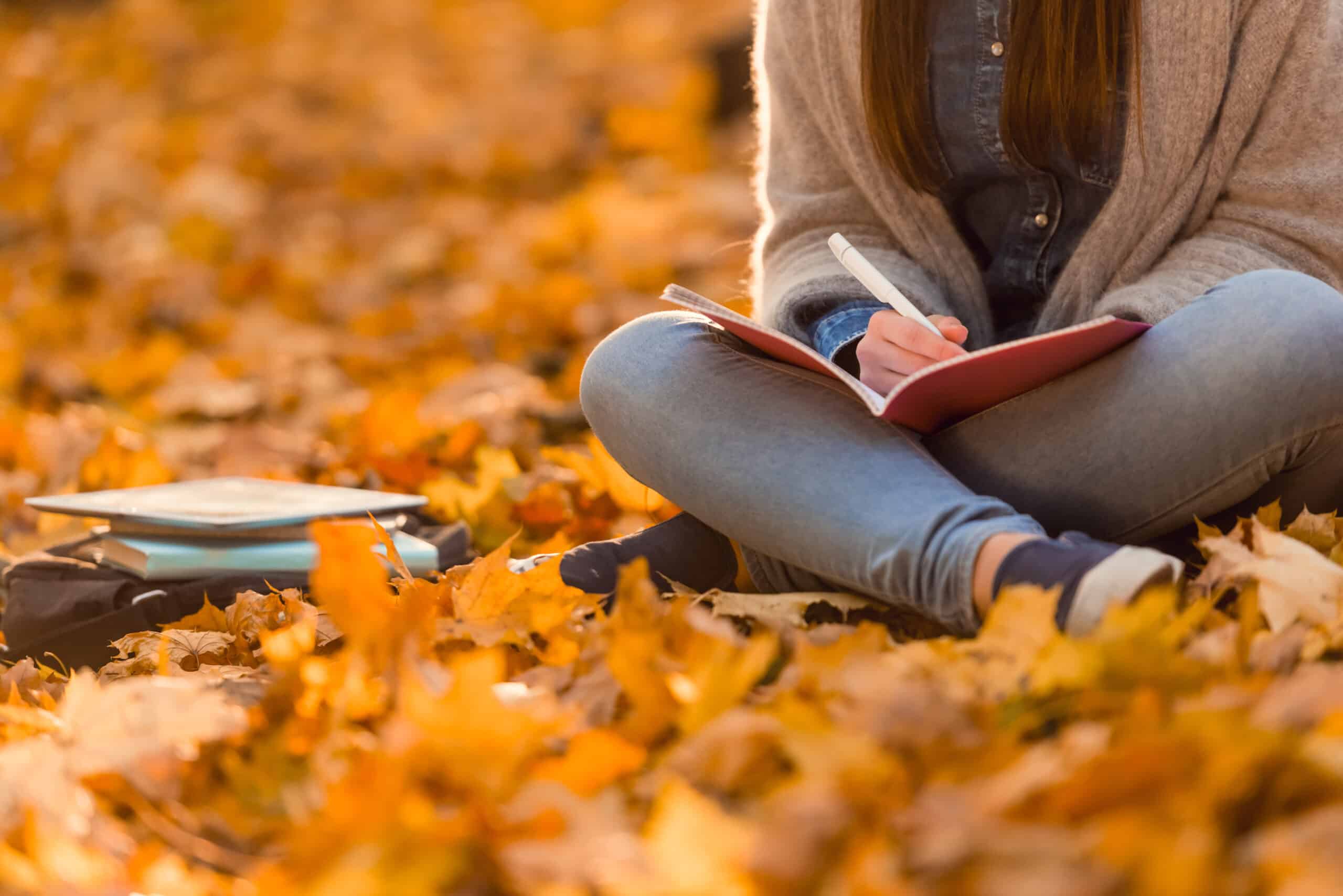 woman sitting on the ground with autumn leaves writing in her journal