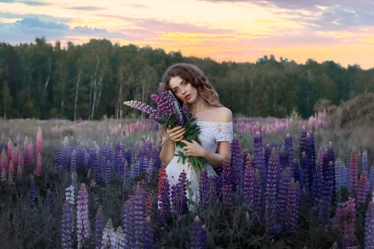 Beautiful, lovely girl among the flowers in the field. Lupins background. Nature and man.