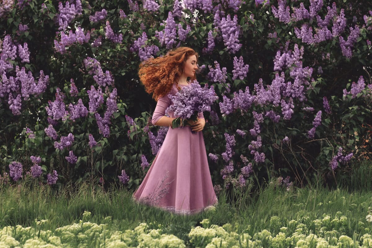 Beautiful young red-haired girl with lilac flowers.