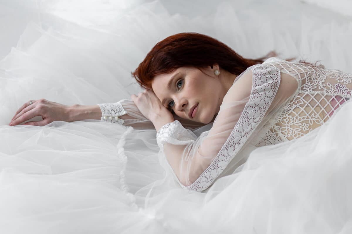 beautiful but weak redhead with a long hair in a white lace dress lying on the bed