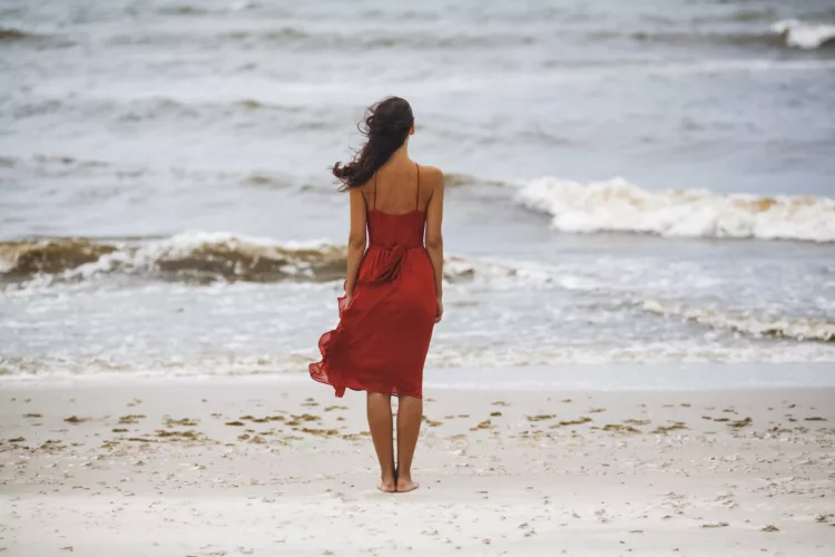 Melancholic woman in a red dress on the beach on a windy day