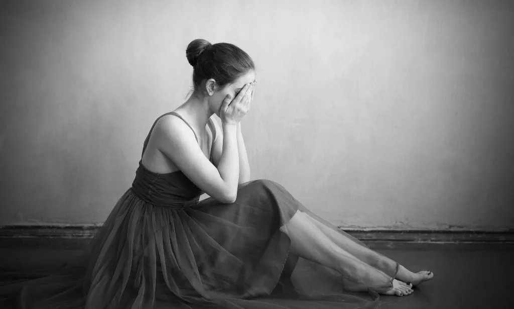 Crying woman in ballet dress on shabby floor.
