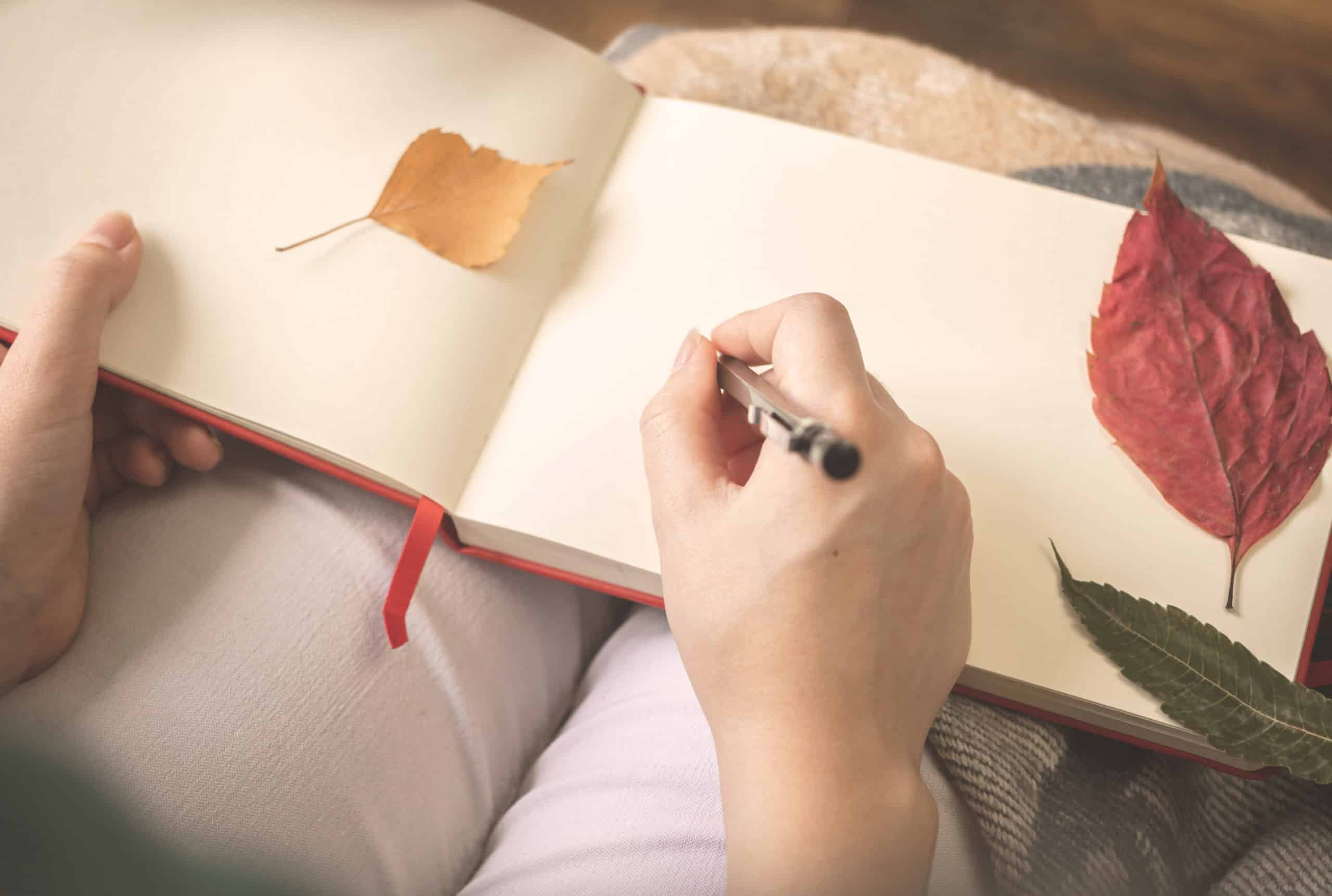 Young woman writes at her old diary with autumn leaves.