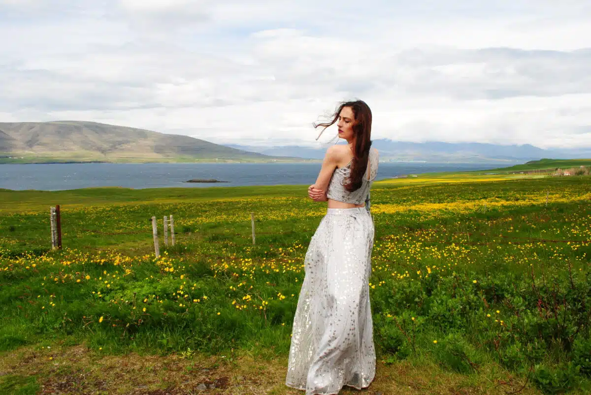 a woman in a white dress is standing near a field of yellow flowers