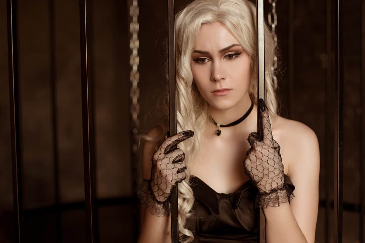 A beautiful blonde woman in a chic evening gown and lacy gloves with an unhappy face and sad emotions. A young girl in a forged cage, a rich captive.