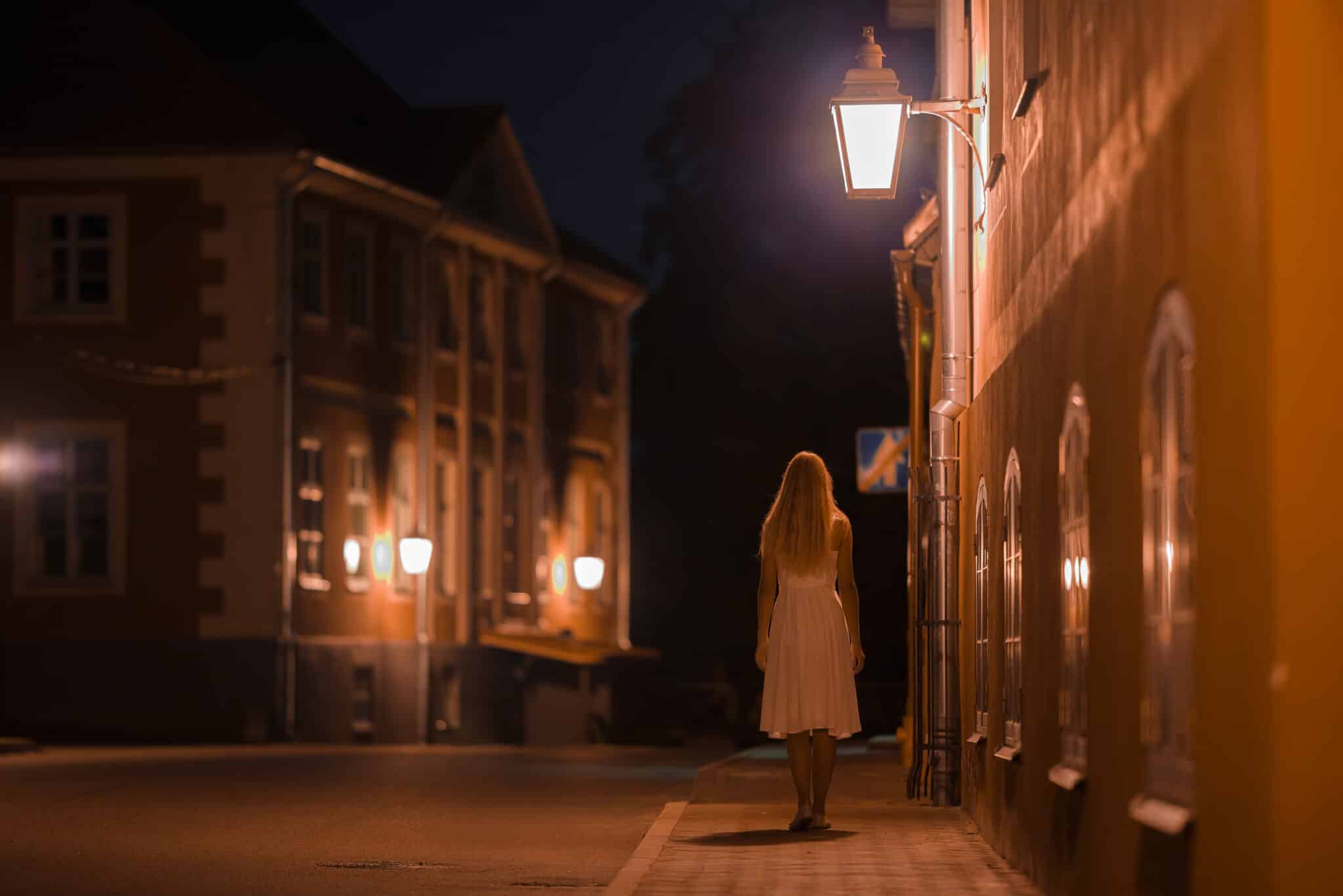 One young alone woman in white dress slowly walking on sidewalk