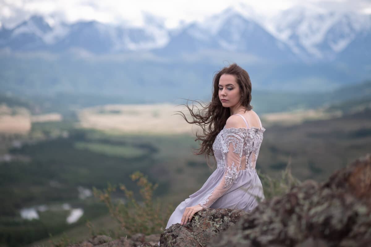 A beautiful lady in a gray dress walks against a mountain range