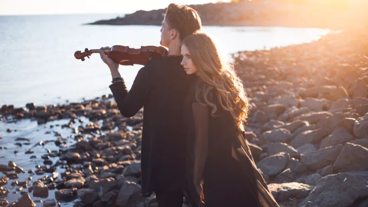 on the seashore, a male violinist playing and a young woman leaning on his back