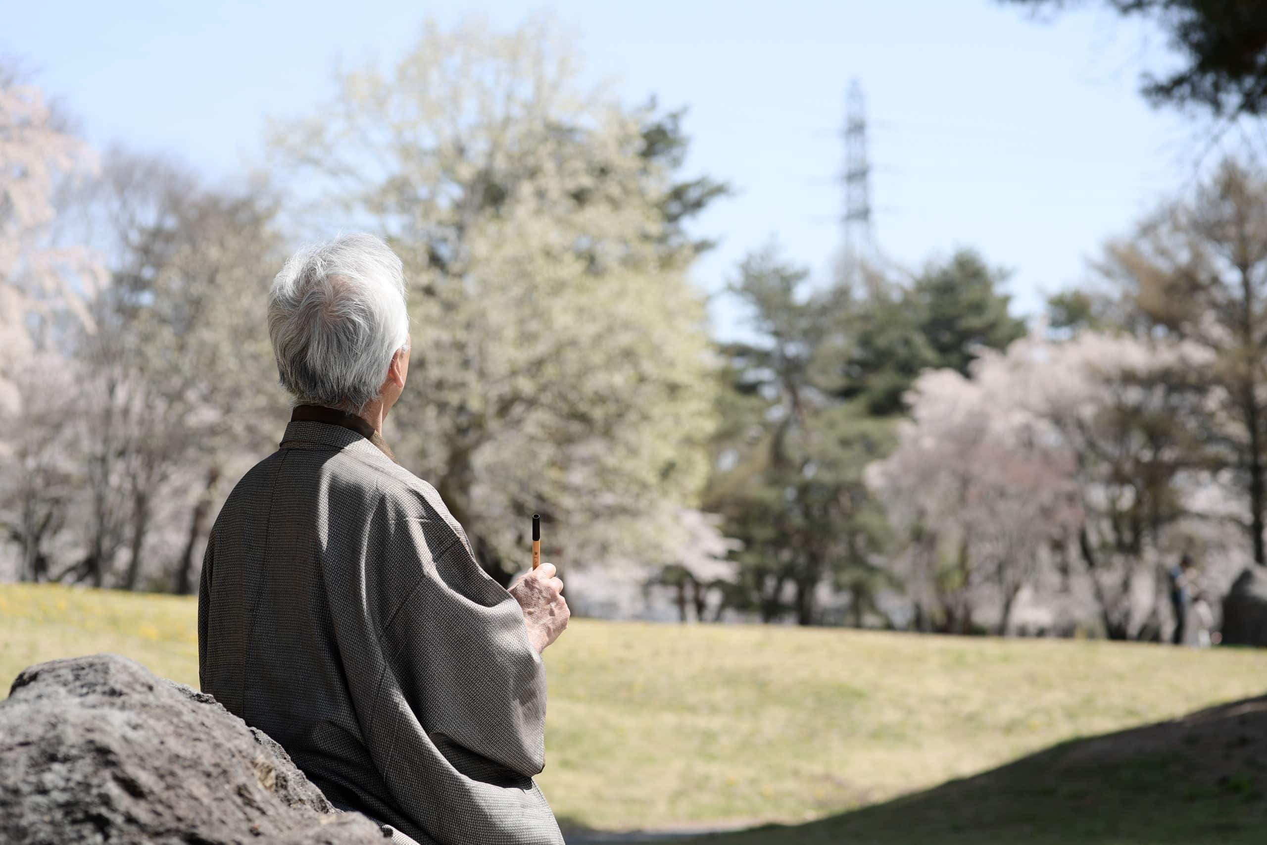 Old Japanese man writing poetry in nature.
