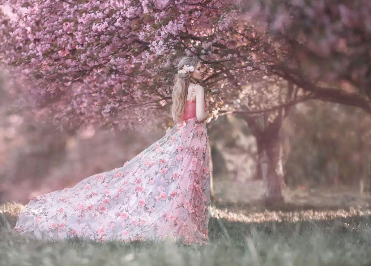 A young princess walks in a blooming garden. Girl in a luxurious pink dress with a train. Fashionable toning.