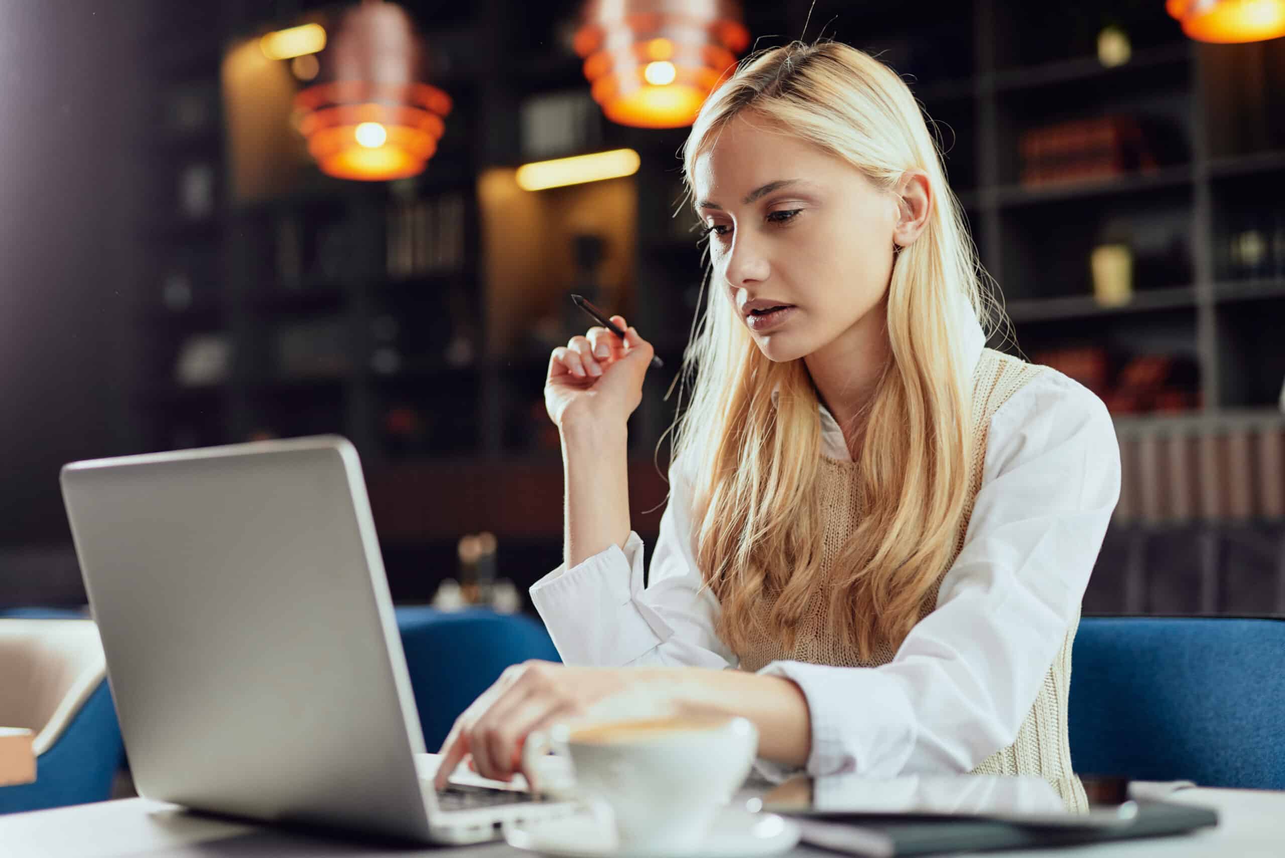 Young blond woman writing working on laptop in cafe