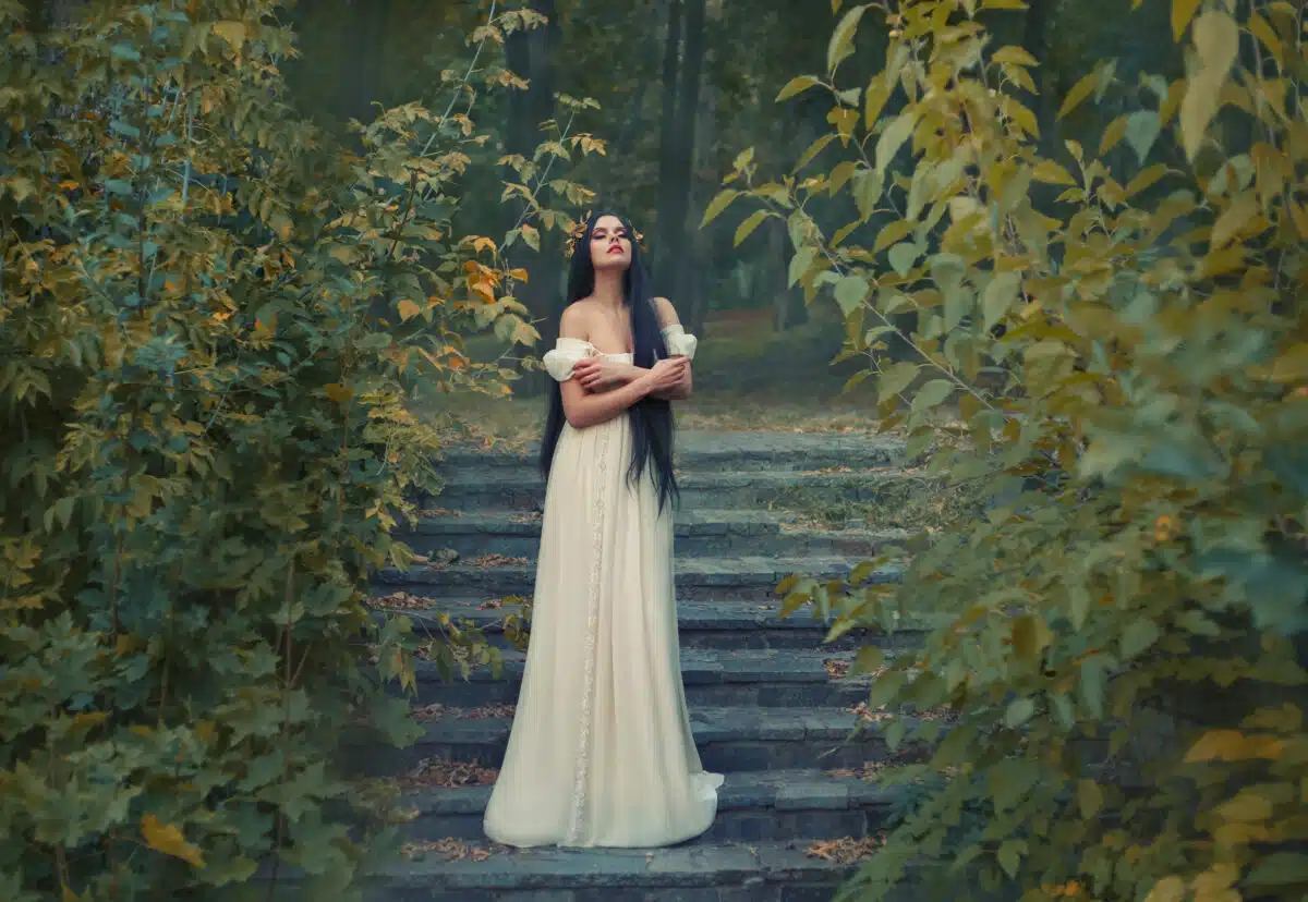A princess with sexually bare shoulders enjoys a moment of silence and loneliness. Black long hair, golden wreath, cream silk vintage dress. runaway