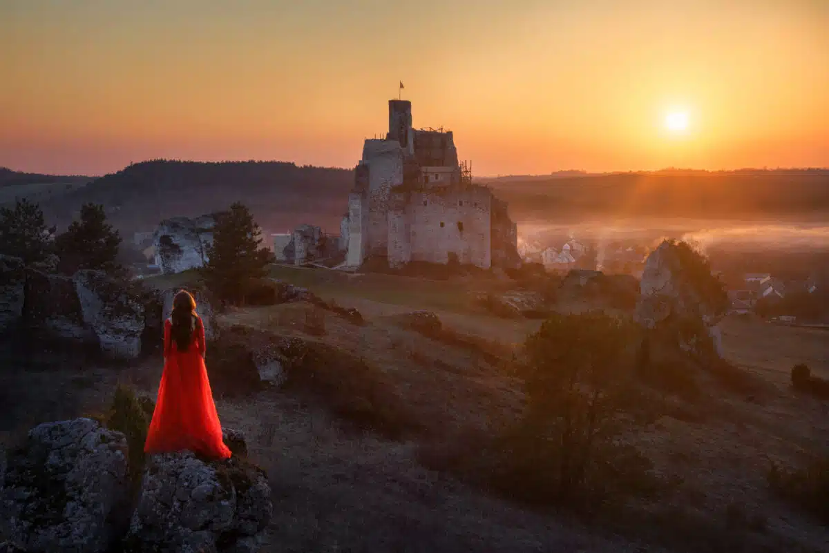 Woman in a red dress standing on a hill looking towards the castle at sunset
