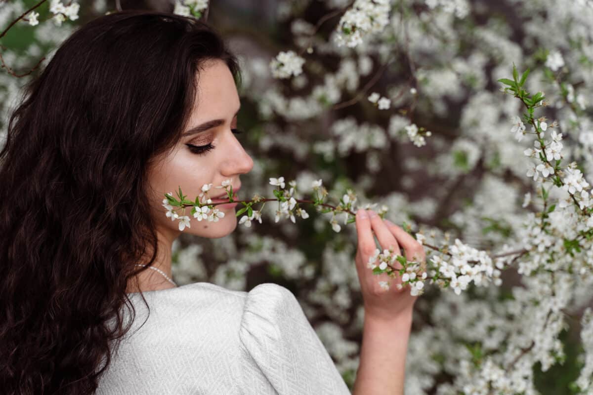 a lady touches and sniffs a branch of a white flowering tree in springtime