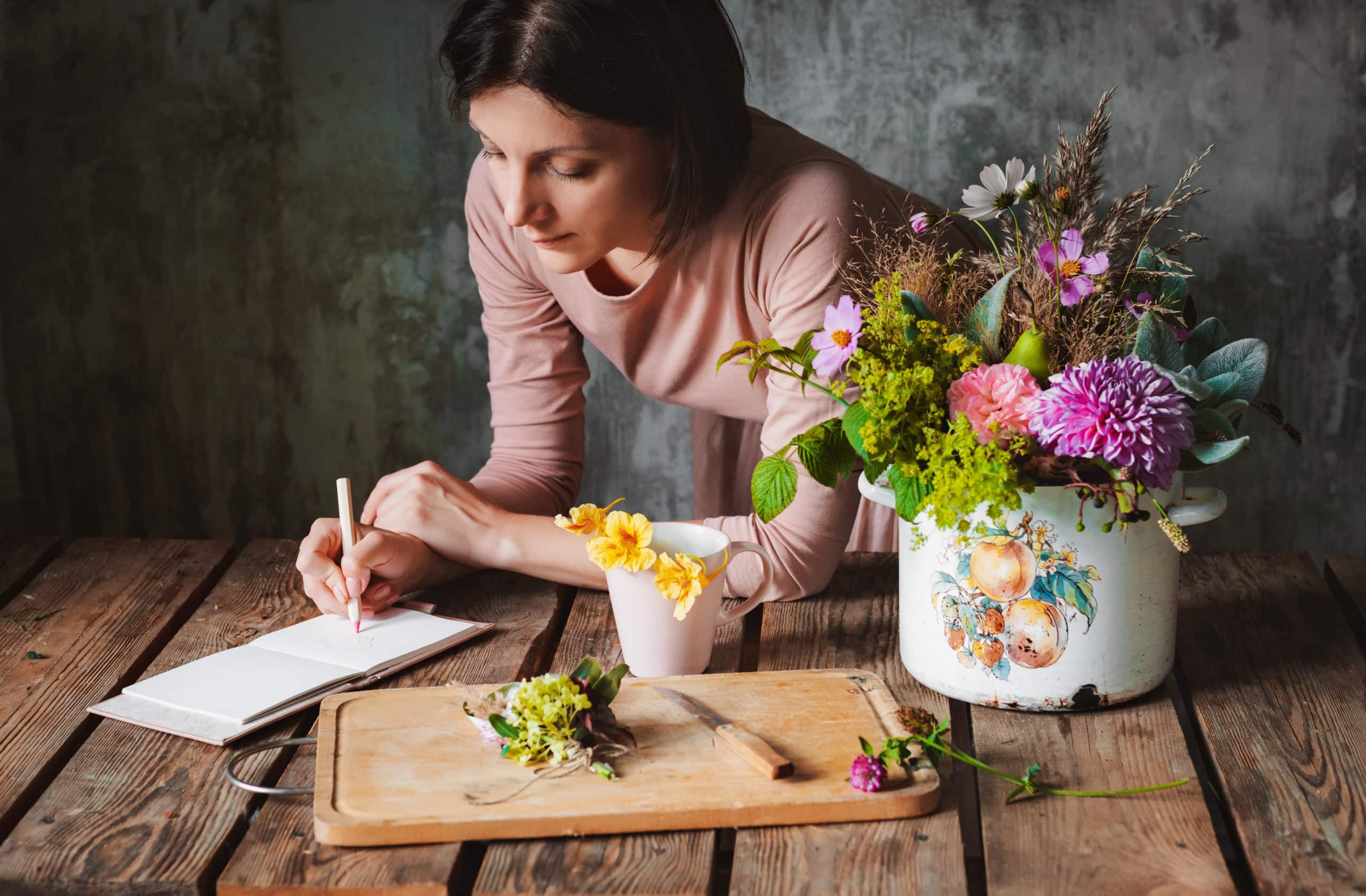 female artist draws a composition of wild flowers in a pot in a rustic style.