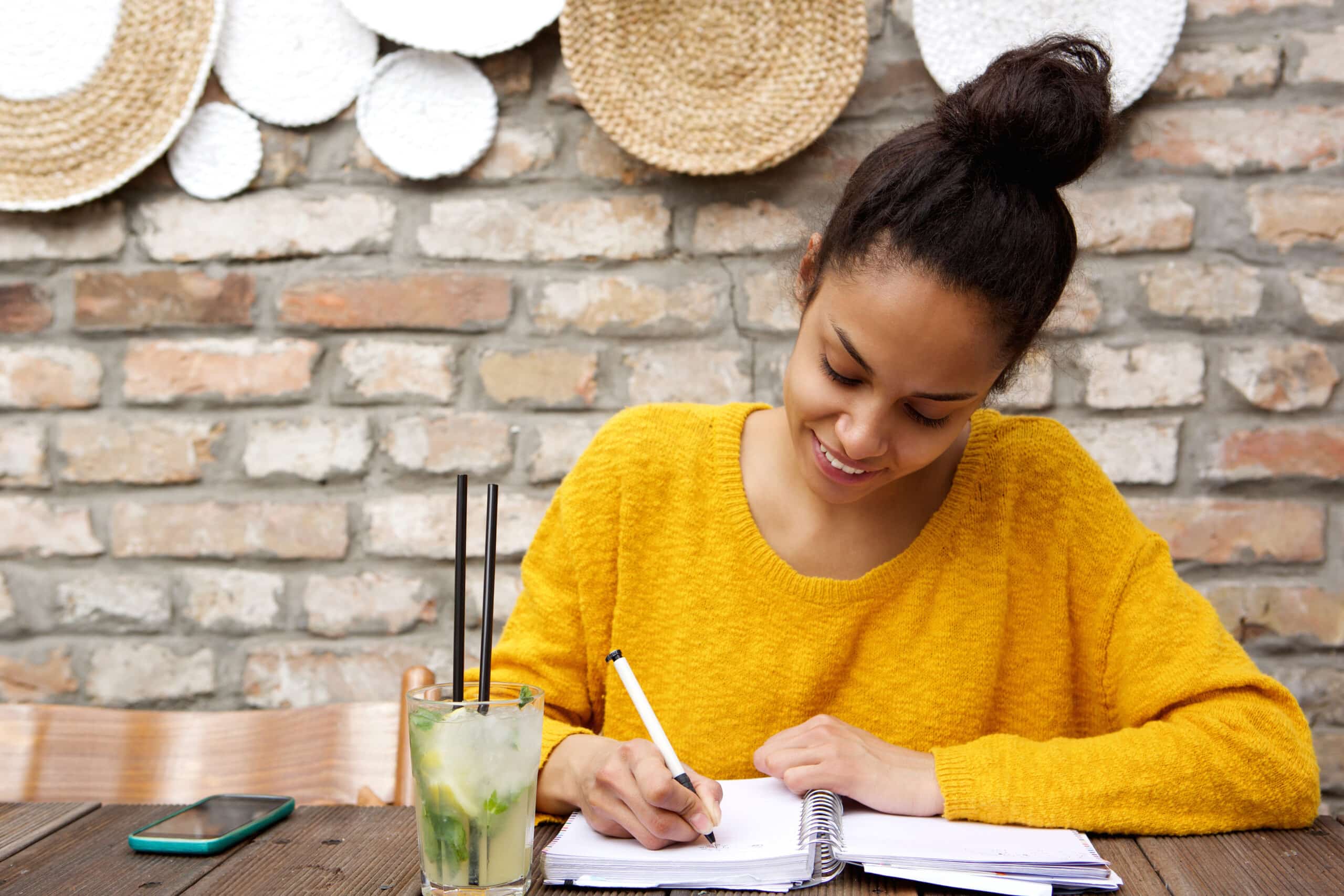 Beautiful young black woman writing at cafe