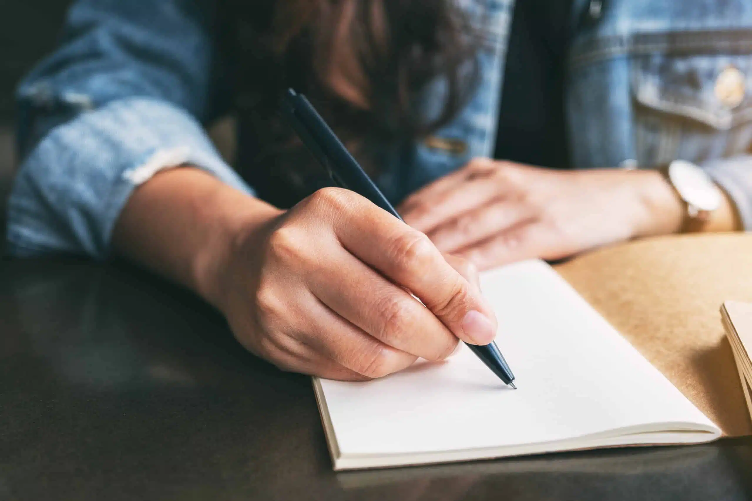 woman writing on a blank notebook on the table.