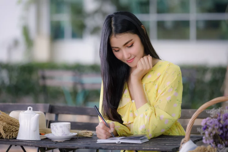 young beautiful asian woman writing on notepad at a table outdoor.