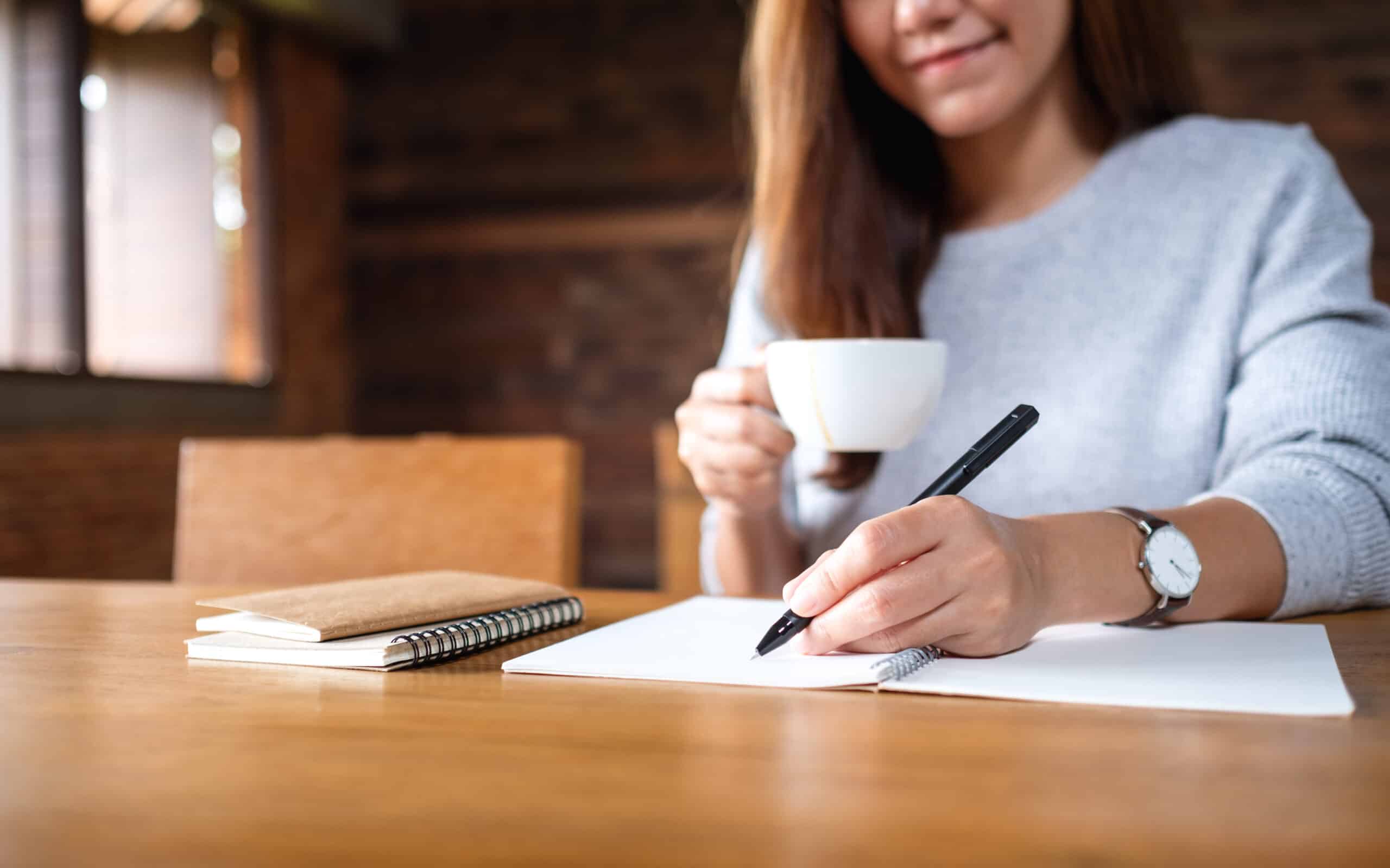 Asian woman drinking coffee and writing on a blank piece of paper.