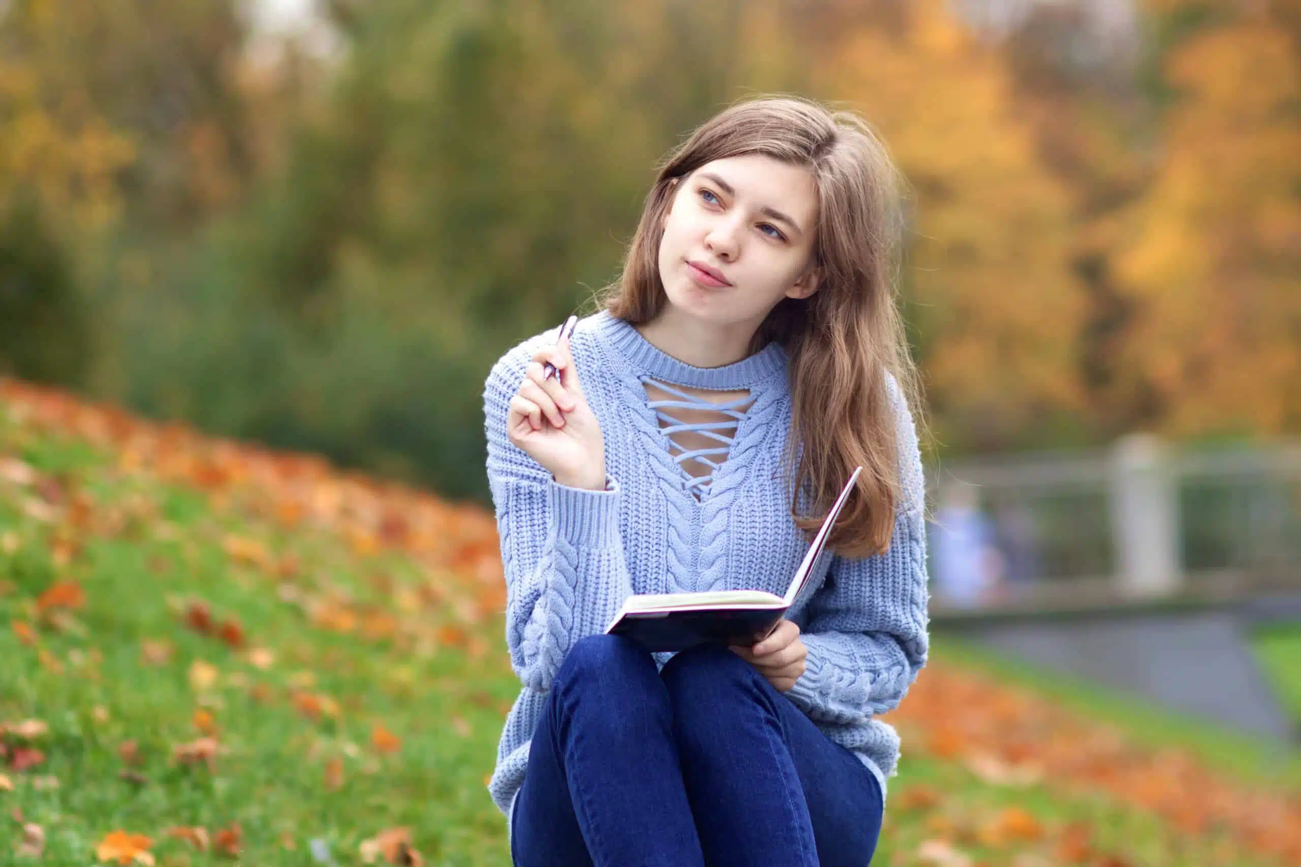 Young beautiful woman writing outdoors in park in pensive mood.