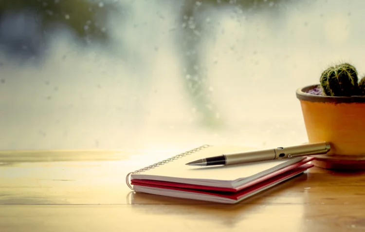 Pen on notebook on window sill, window with water drops from the rain