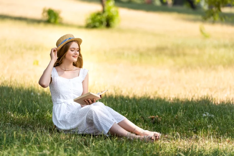 beautiful girl in white dress touching straw hat and holding a book