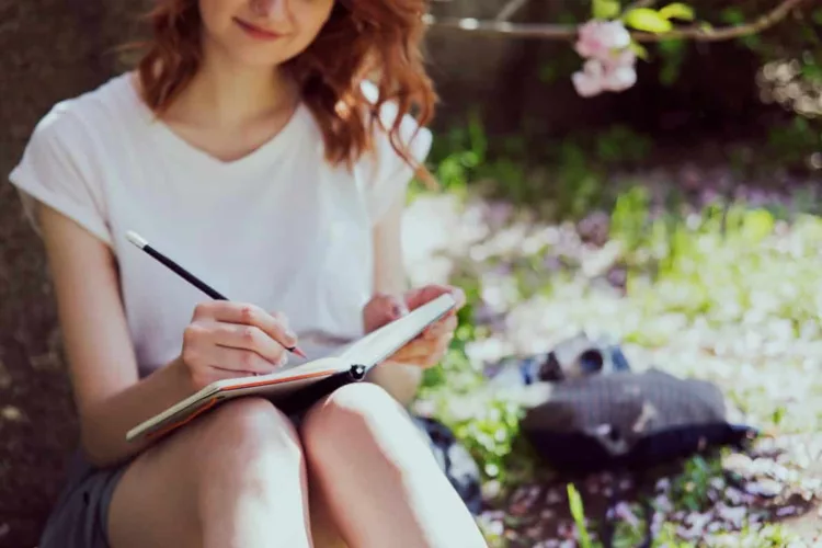 Young beautiful redhead girl in white shirt writing outdoors