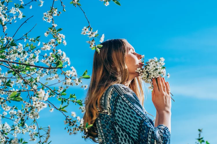 young girl in cherry garden smelling a bouquet of flowers, with the bright blue sky above