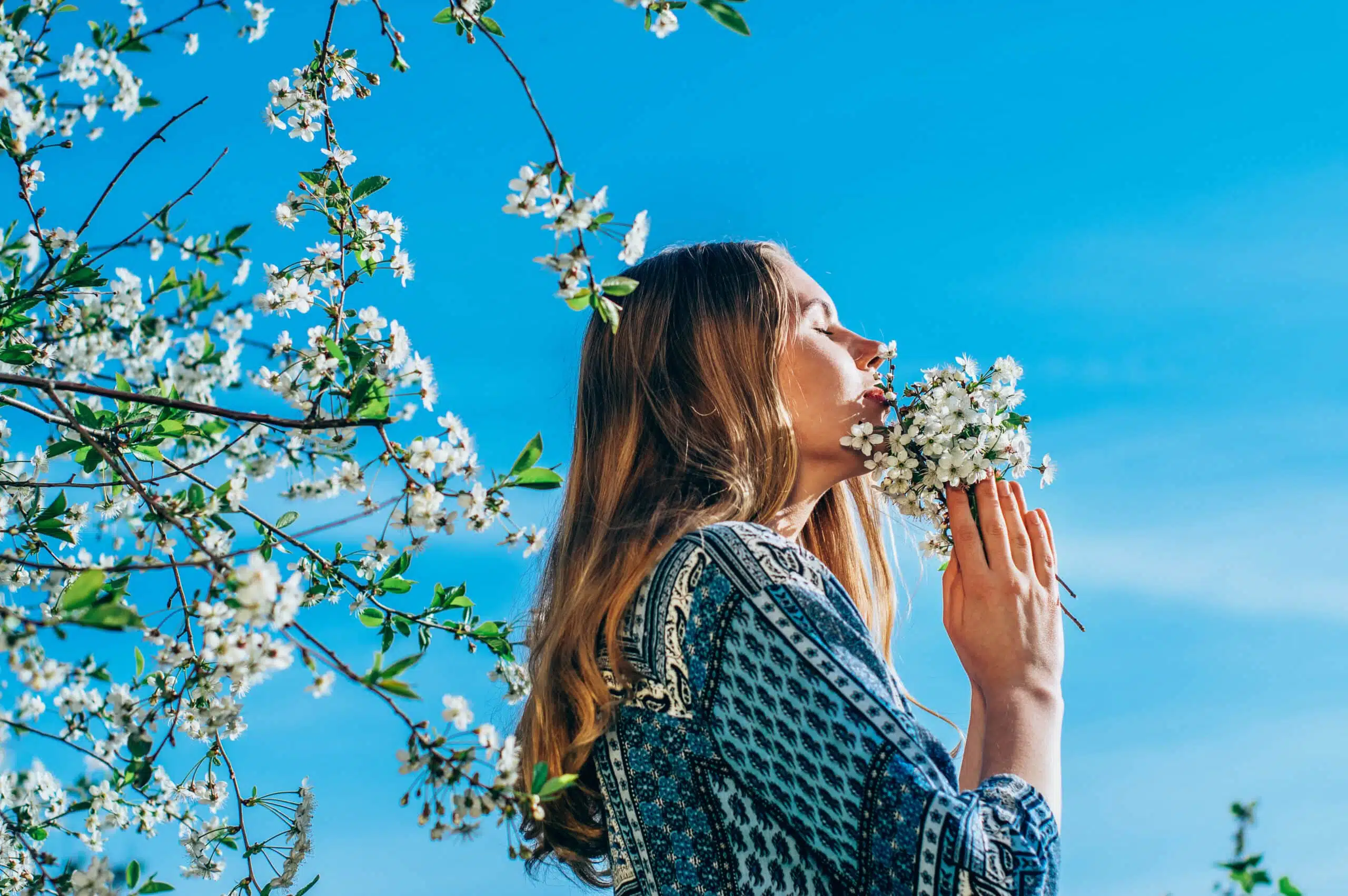 young girl in cherry garden smelling a bouquet of flowers, with the bright blue sky above