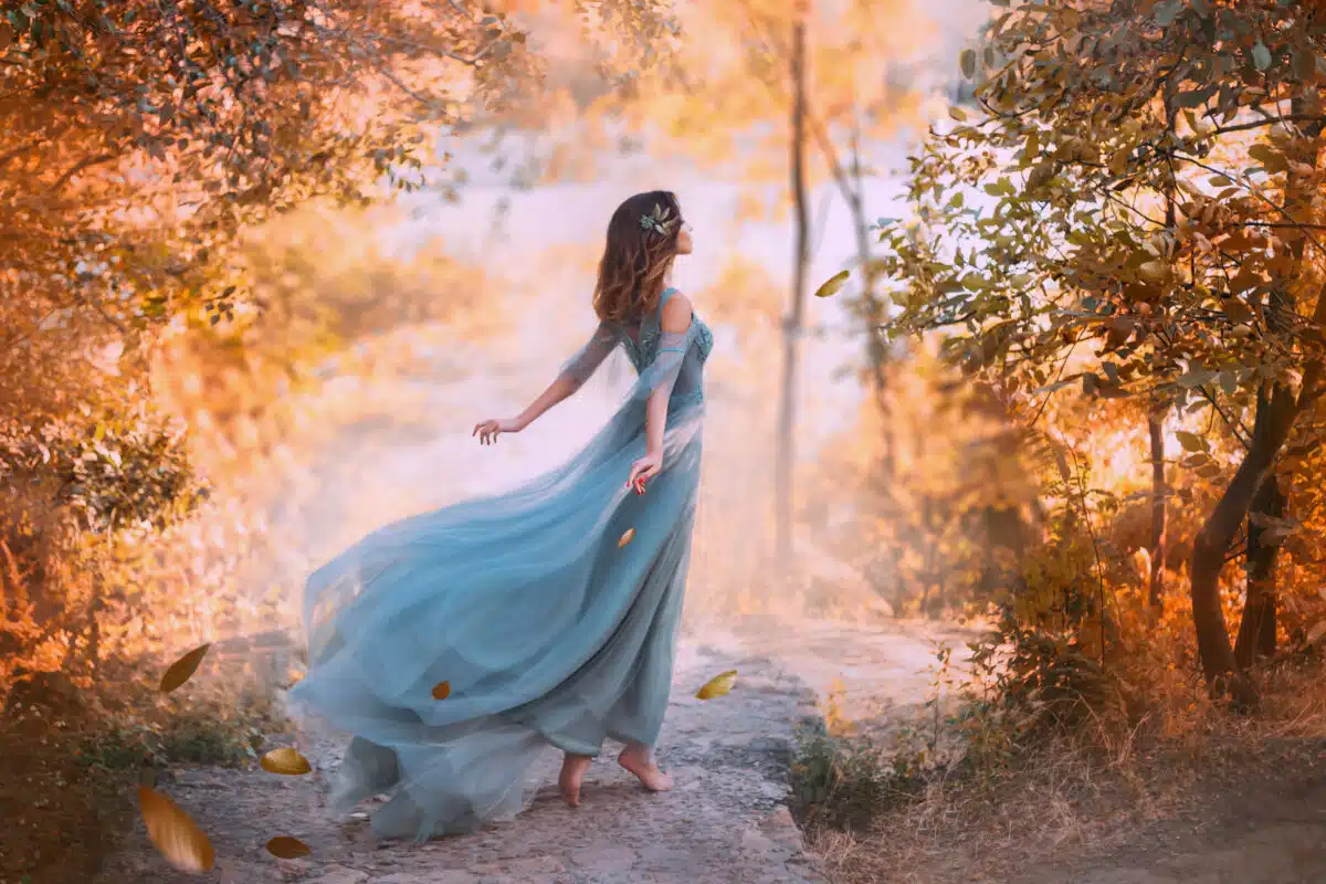fantasy girl in sky blue turquoise dress with long flying train with fallen autumn leaves flying to ground