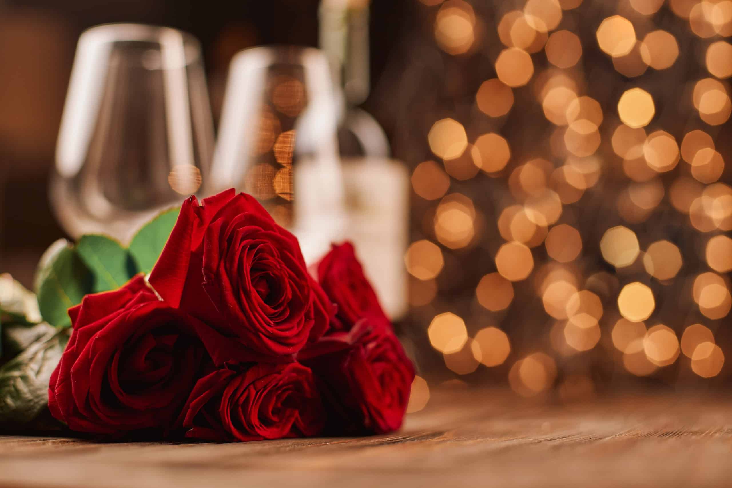 A bouquet of roses and wine glasses on a festive background.