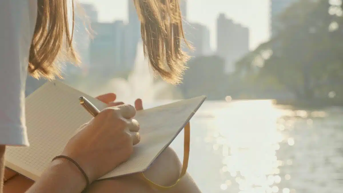 Young woman sitting on the bench in park and writing in diary, close-up.