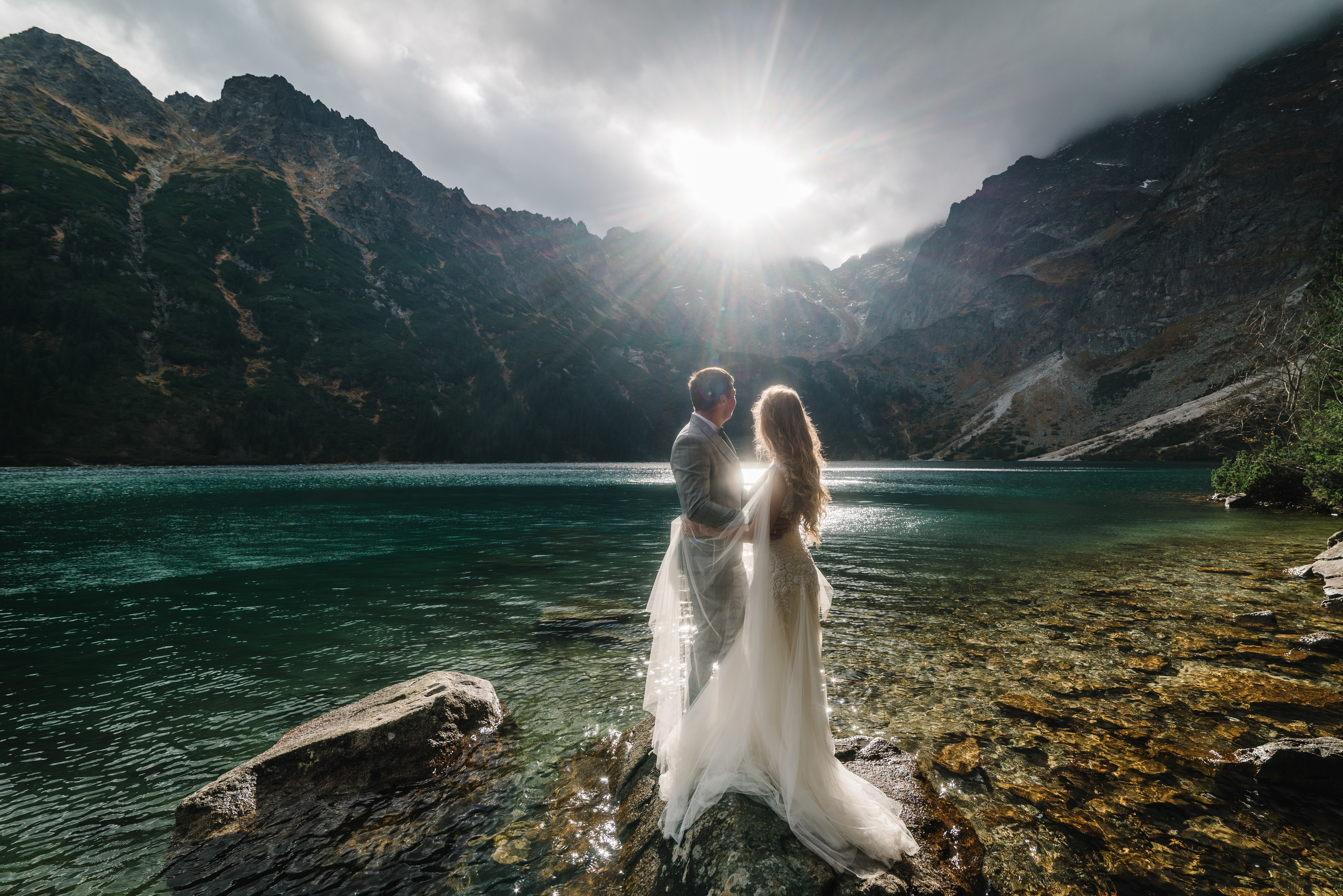 lovely couple holding each other near the lake in the mountains looking toward the sunrise