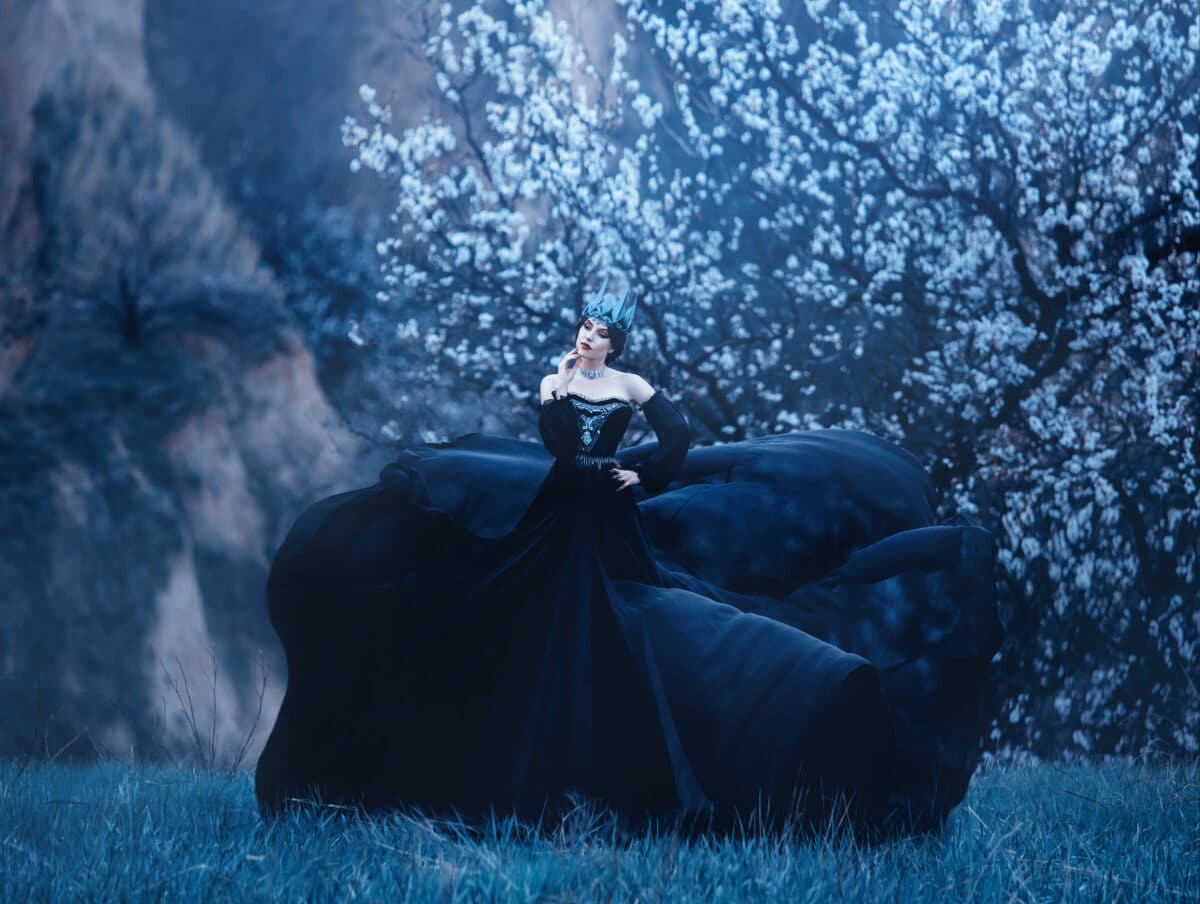 queen of night in luxurious black dress with long flying train, lady with dark makeup, metal cold jewelry and crown, mysterious priestess near blossoming tree, gloomy gothic image of jellyfish.