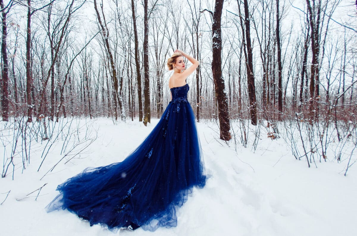 lady in a blue gown standing in the snow in the woods
