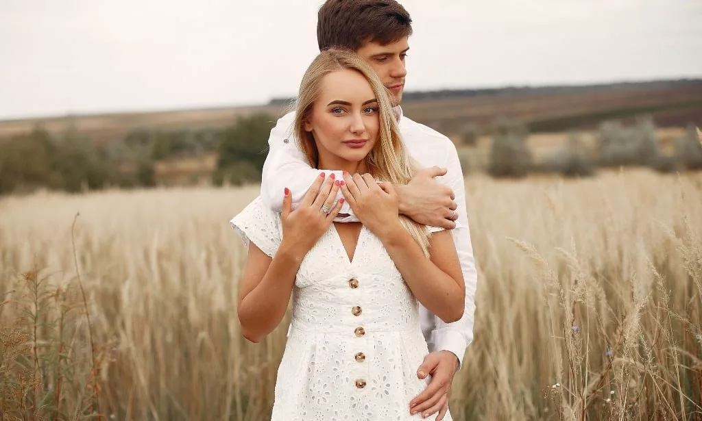 Cute couple in a field, husband hugging his wife from behind.