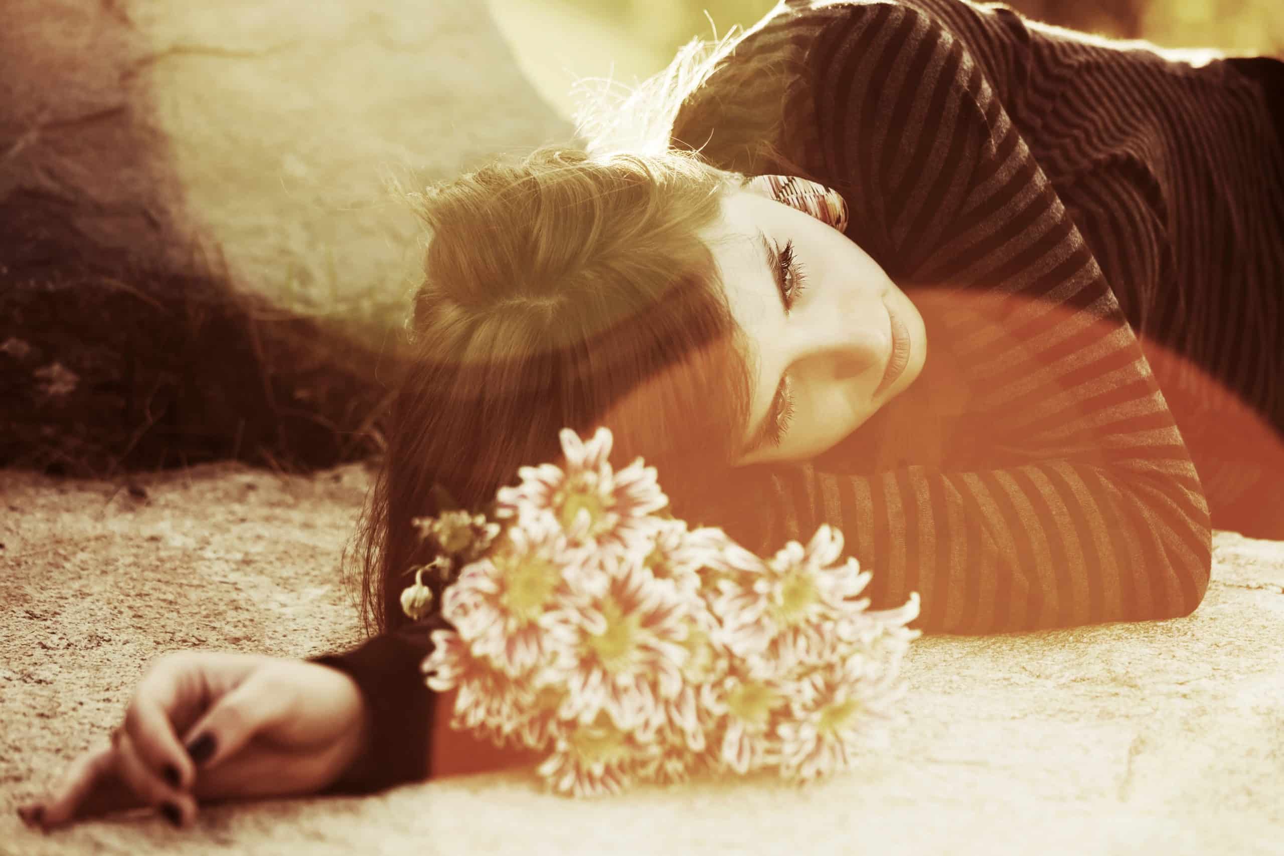 Sad young woman lying on the ground, white flowers above her head.