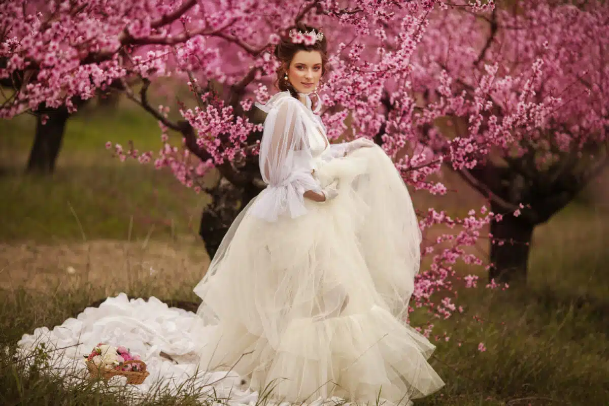 beautiful woman with dark hair in elegant white dress in the pink spring garden