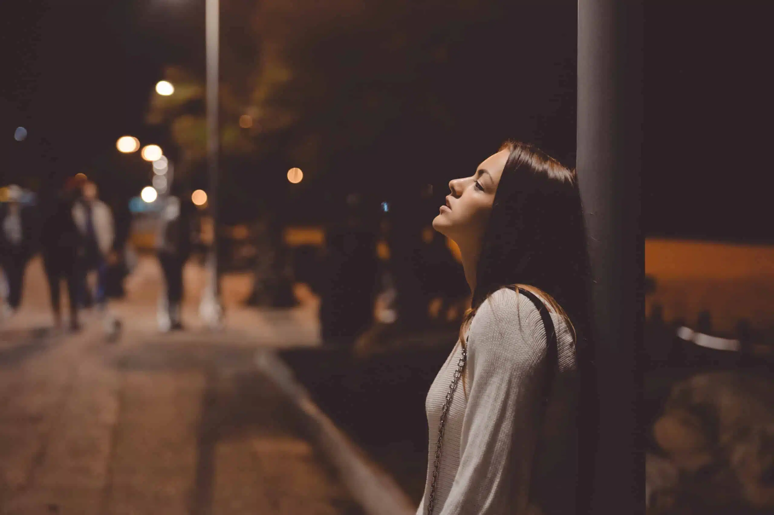 Portrait of beautiful young lady looking up, city street in the night, evening lights bokeh background outdoors
