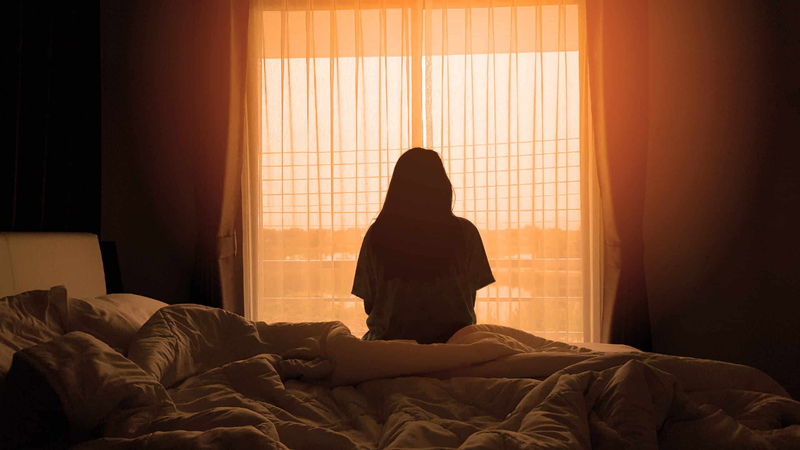 silhouette of woman sitting on the bed beside the windows with s