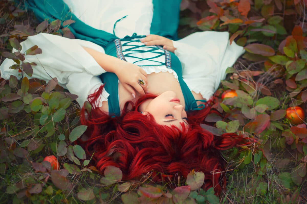 wonderful red-haired princess is lying on the ground, torn with leaves, gently laid her hand, dressed in a long emerald feminine silk and white dress, the apples fell out of the basket, sleeping girl