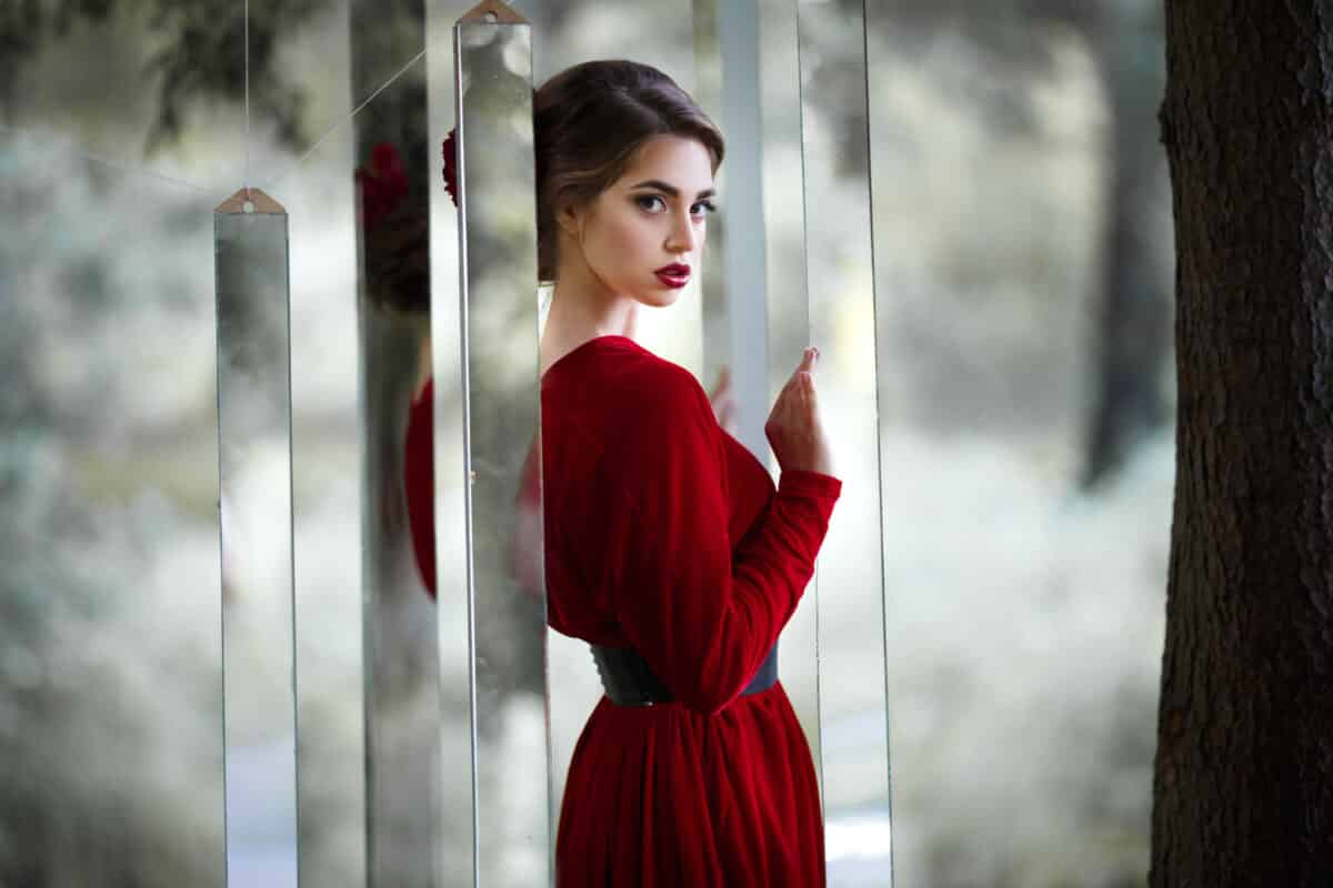 a mysterious girl in a long red dress stands by mirrors in the woods