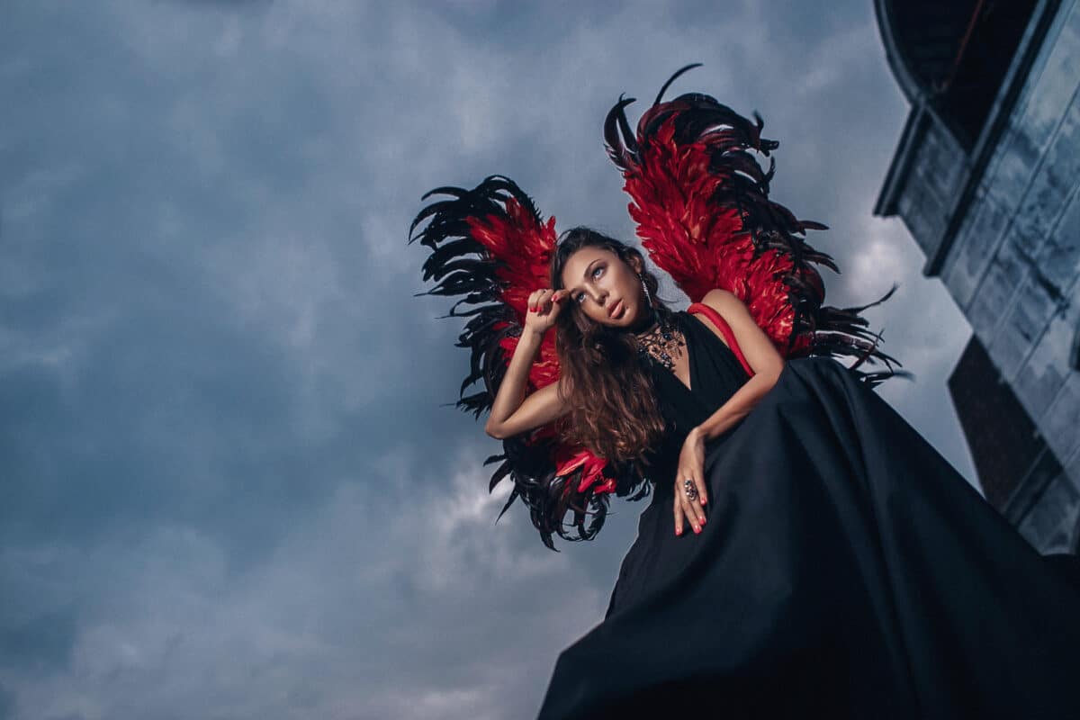 a dark angel with red and black wings and the dark sky above her