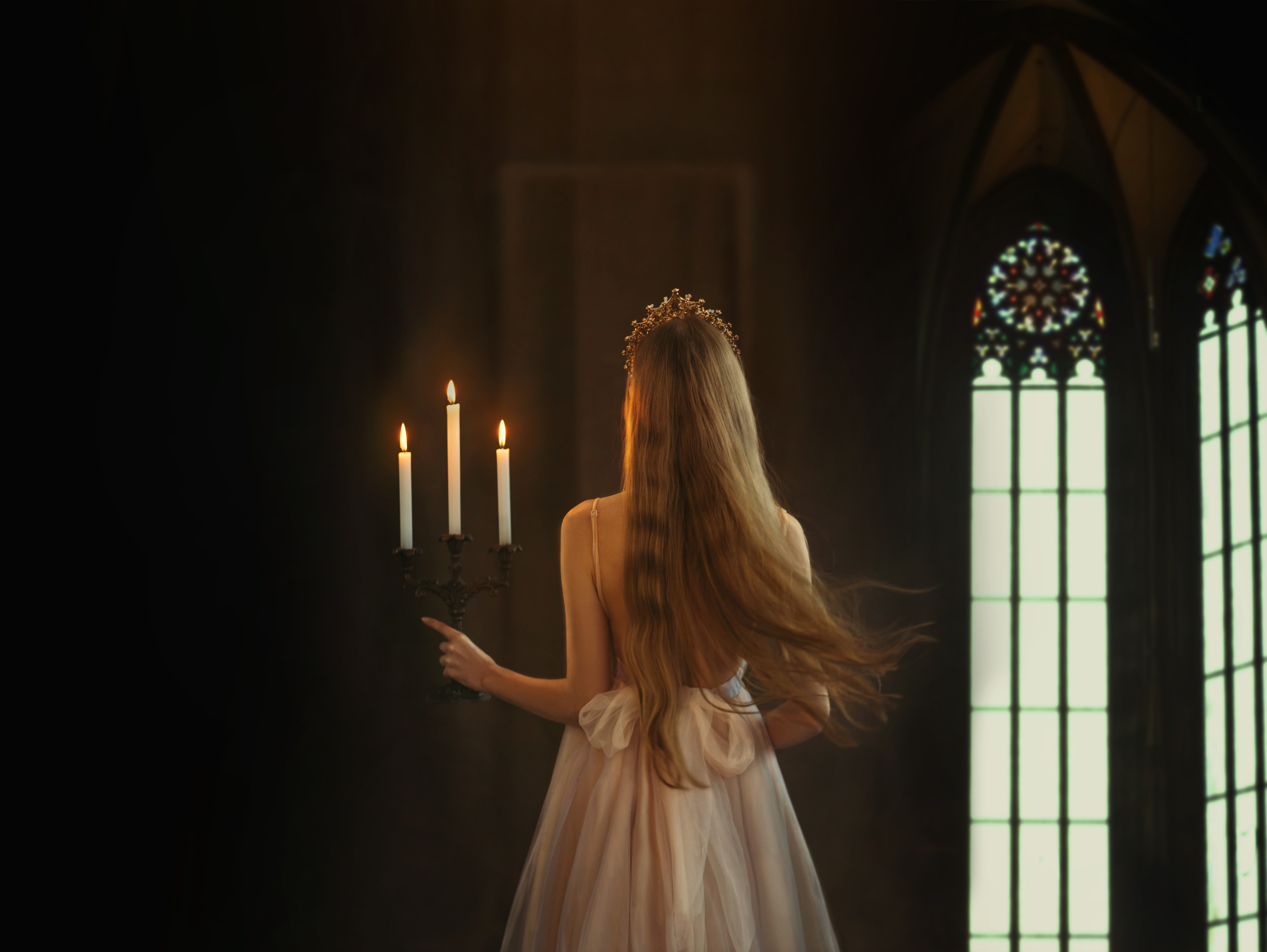 Mysterious art medieval girl princess walks in dark gothic room. Woman queen is holding candlestick with burning candles in hand. 