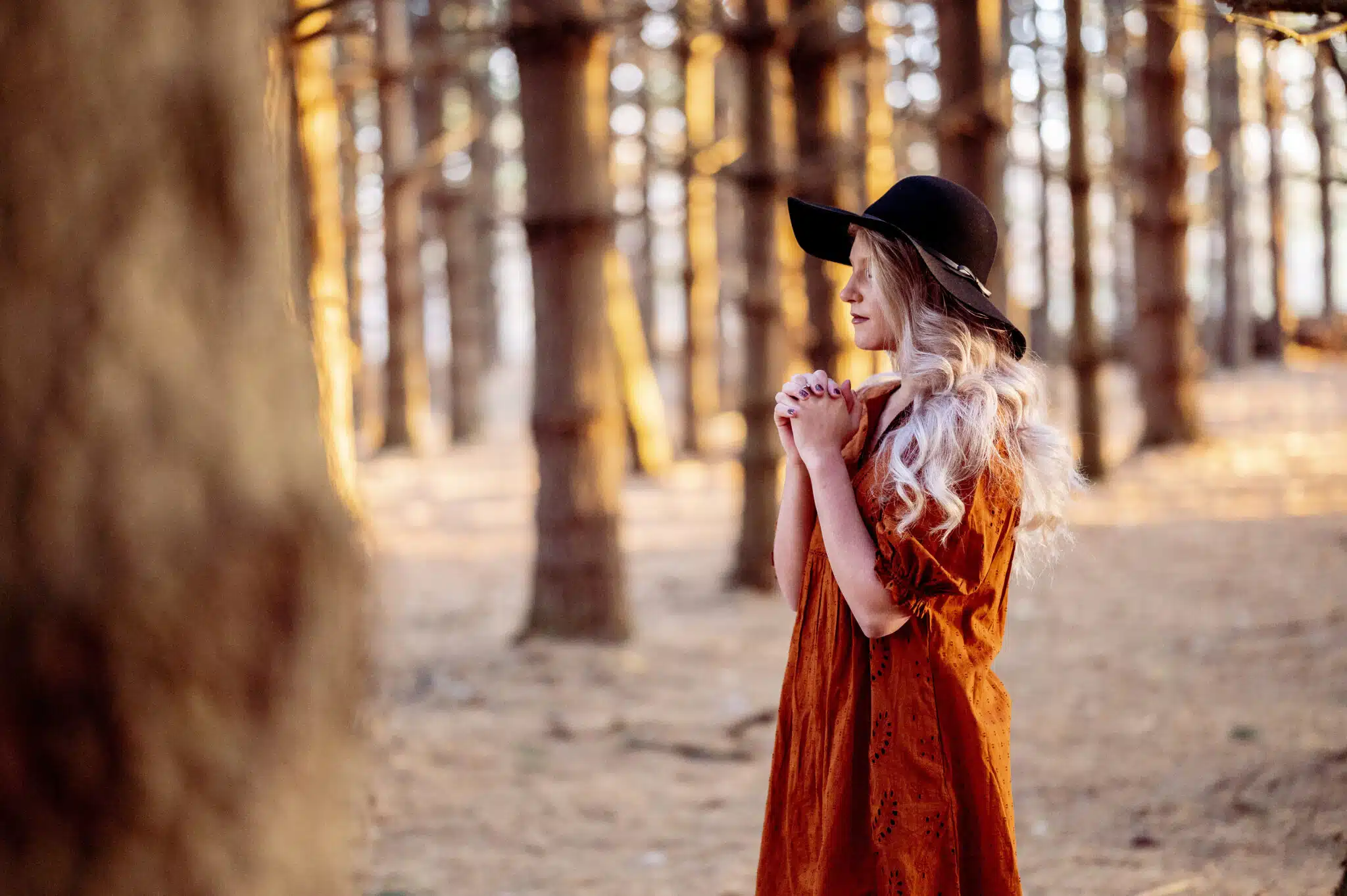 Young Caucasian female in a stylish black hat praying in the scenic forest, autumn mood