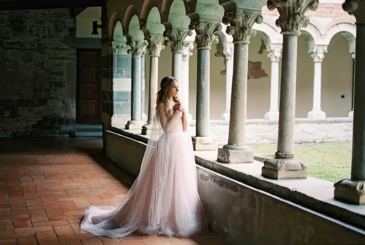Bride stands with her arms folded across her chest on the terrace of an old villa.
