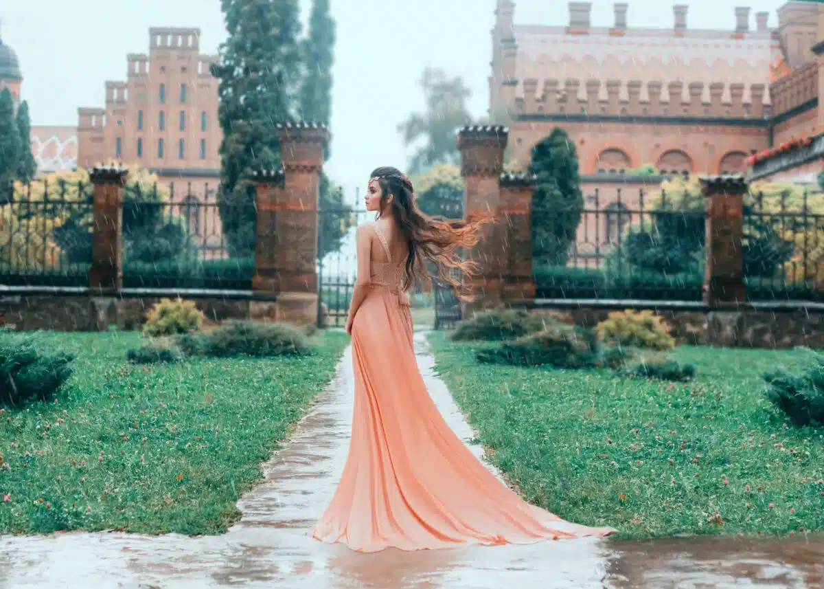 Lonely Attractive brunette woman walks in the rain near the stator castle. Young princess in a pink wet dress with a train. Hair fluttering, flying in the wind. Autumn sad landscape.