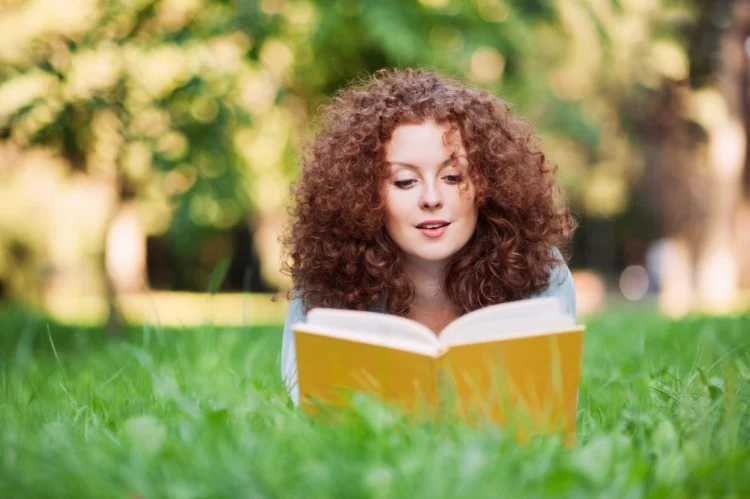 Beautiful redhead reading a book in a summer green park