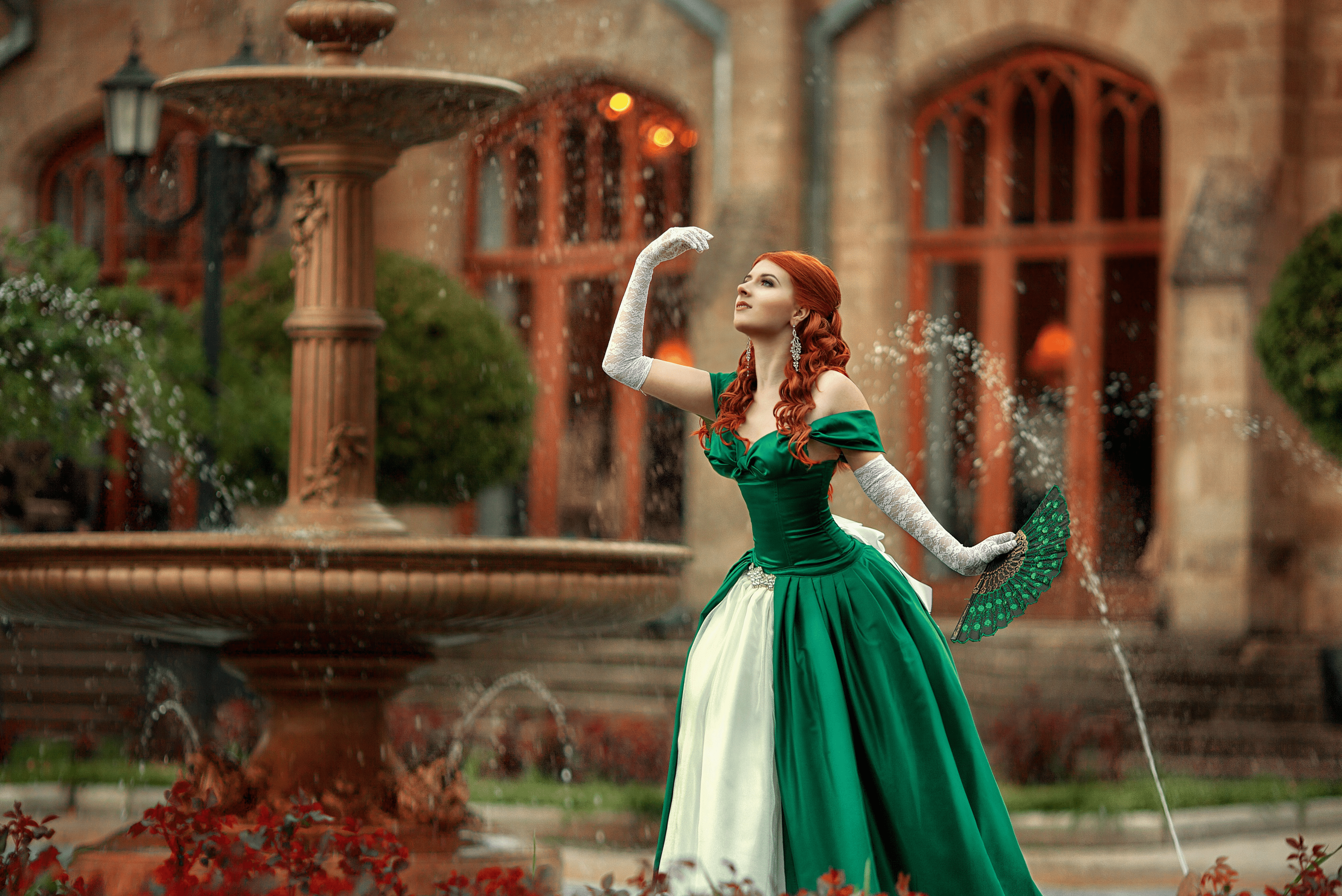 A beautiful red-haired girl in a ball gown is walking by the fountains.