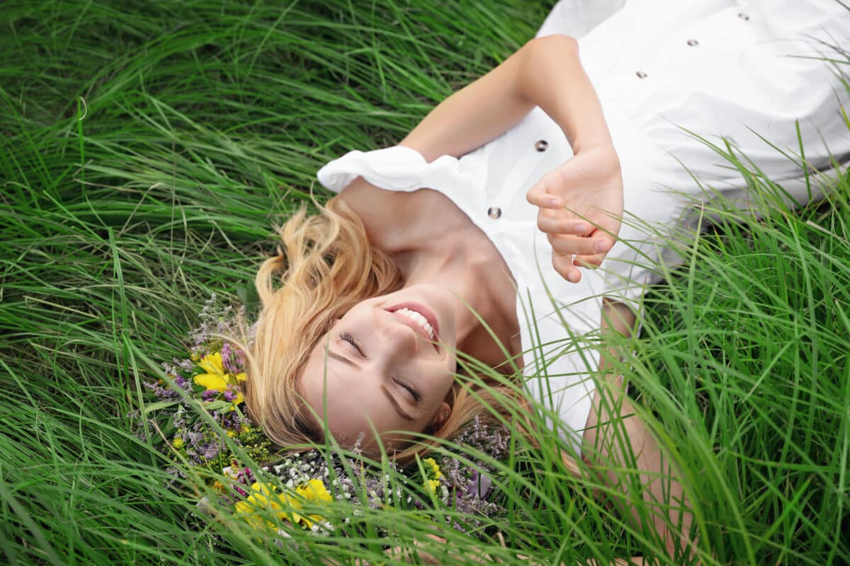 a young woman wearing a head wreath made of beautiful flowers lying on green grass
